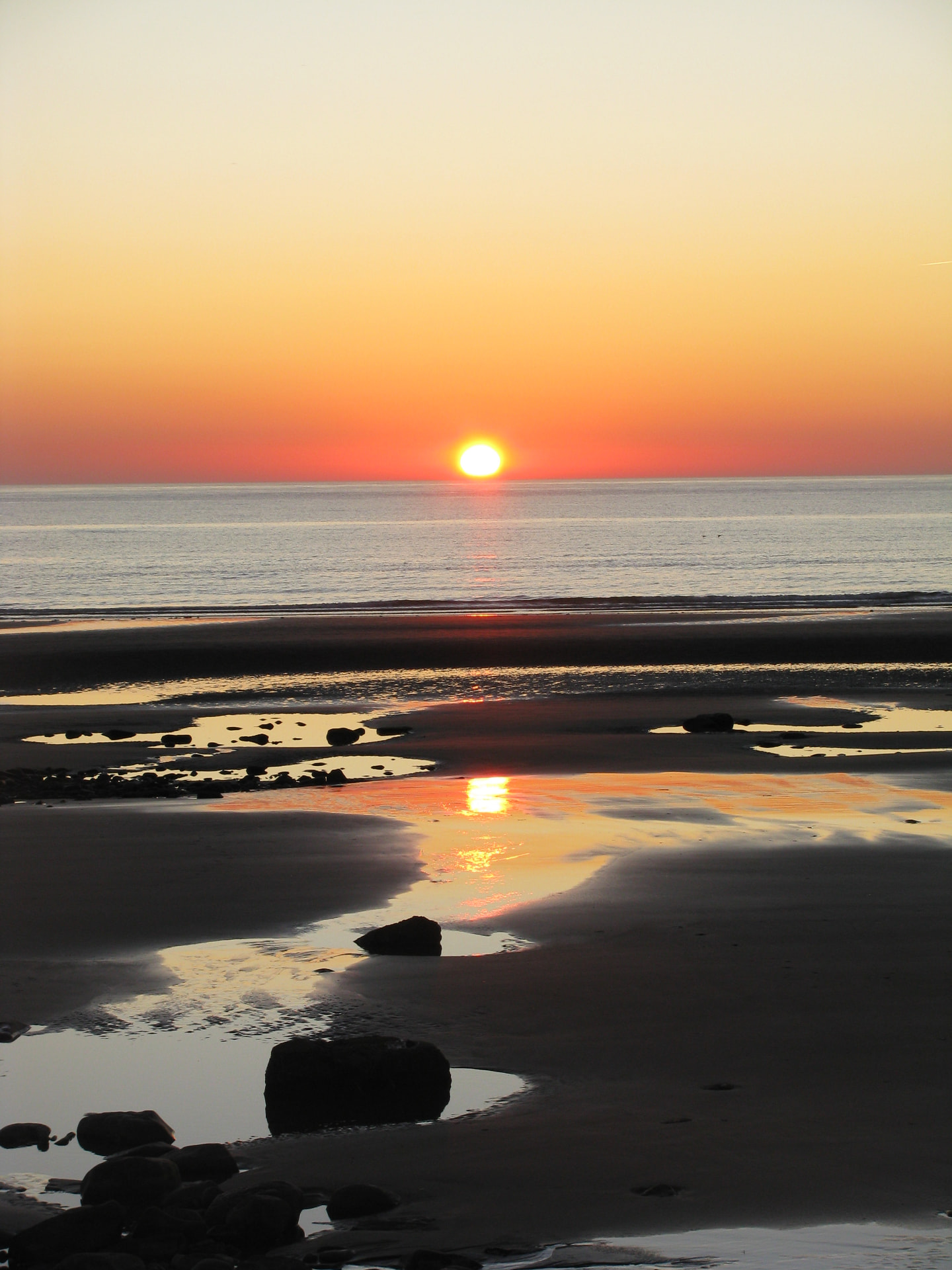 Sun setting over a calm ocean, reflected on wet sand and tidal pools